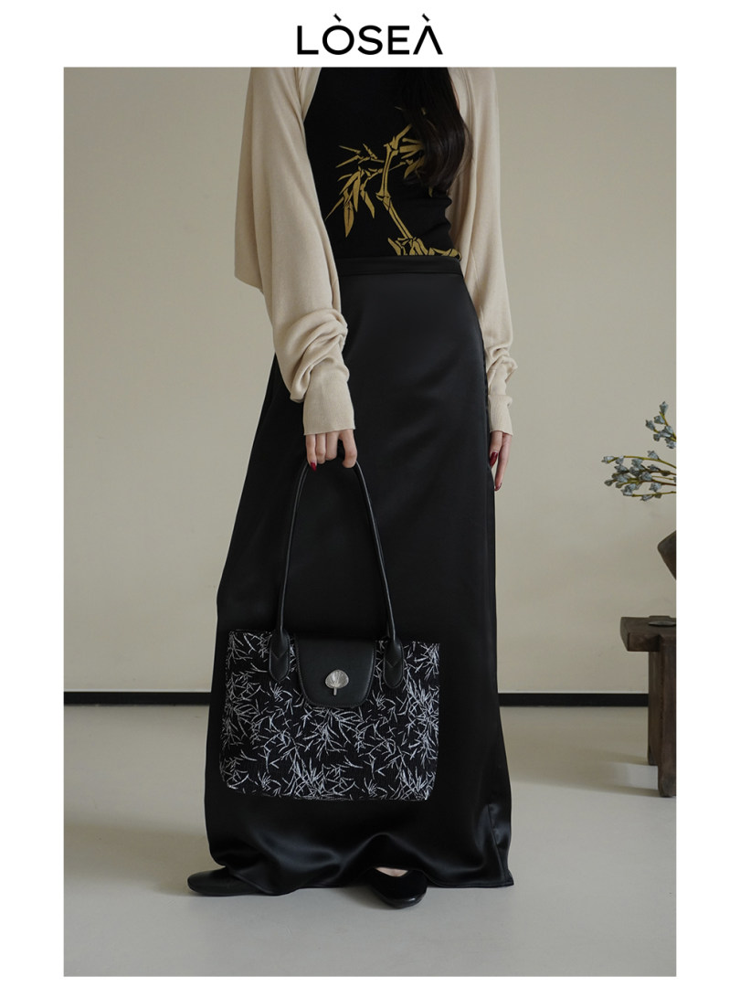 Model wearing a black outfit and holding a patterned black tote bag