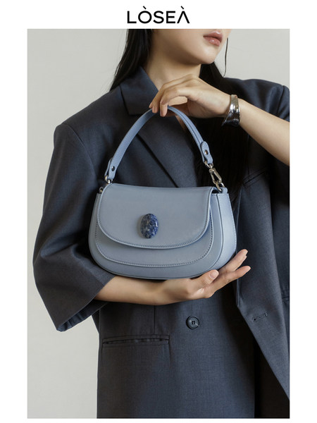 Light blue shoulder handbag held by a model in a dark blazer