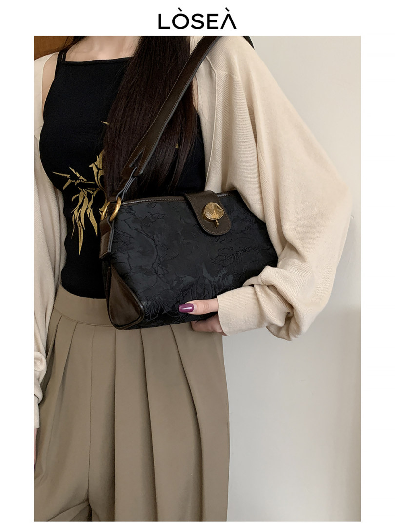 Black crossbody handbag worn by a model with a beige outfit
