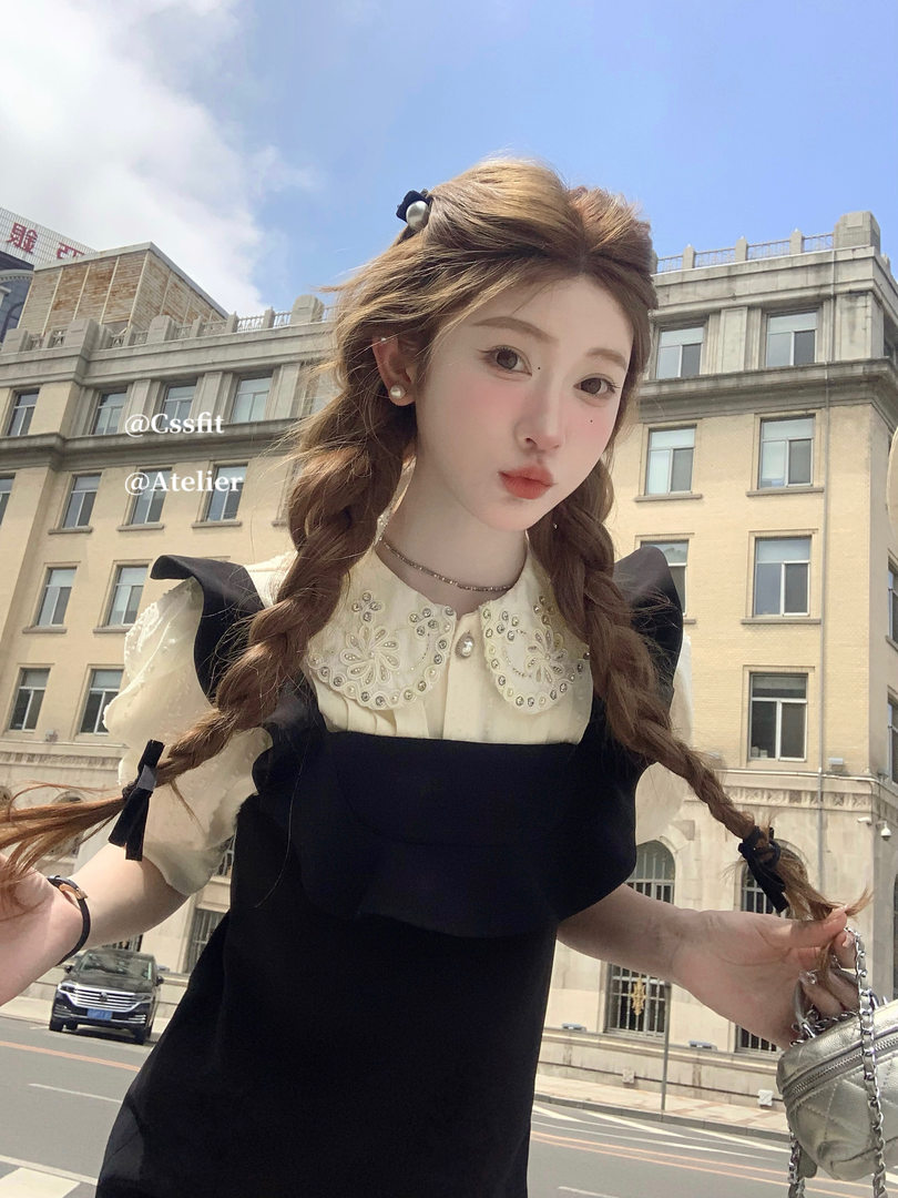 Black pinafore dress layered over a cream embellished blouse on a model outdoors