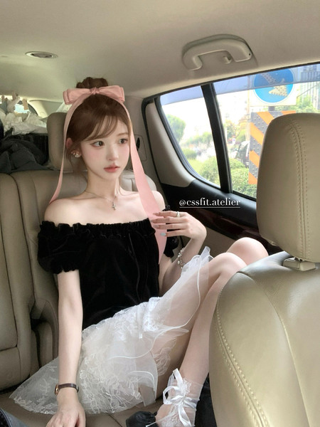 Woman wearing a black off-shoulder top with a white lace skirt and pink ribbon headband in a car