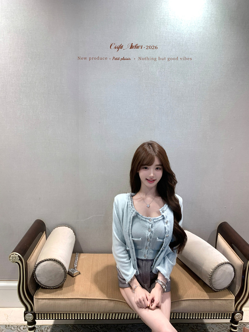 Woman wearing a light blue cardigan and matching top with gray shorts on a sofa