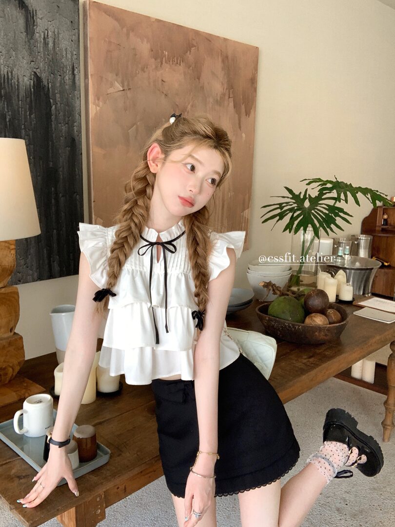Model wearing a white ruffled sleeveless top with a black skirt