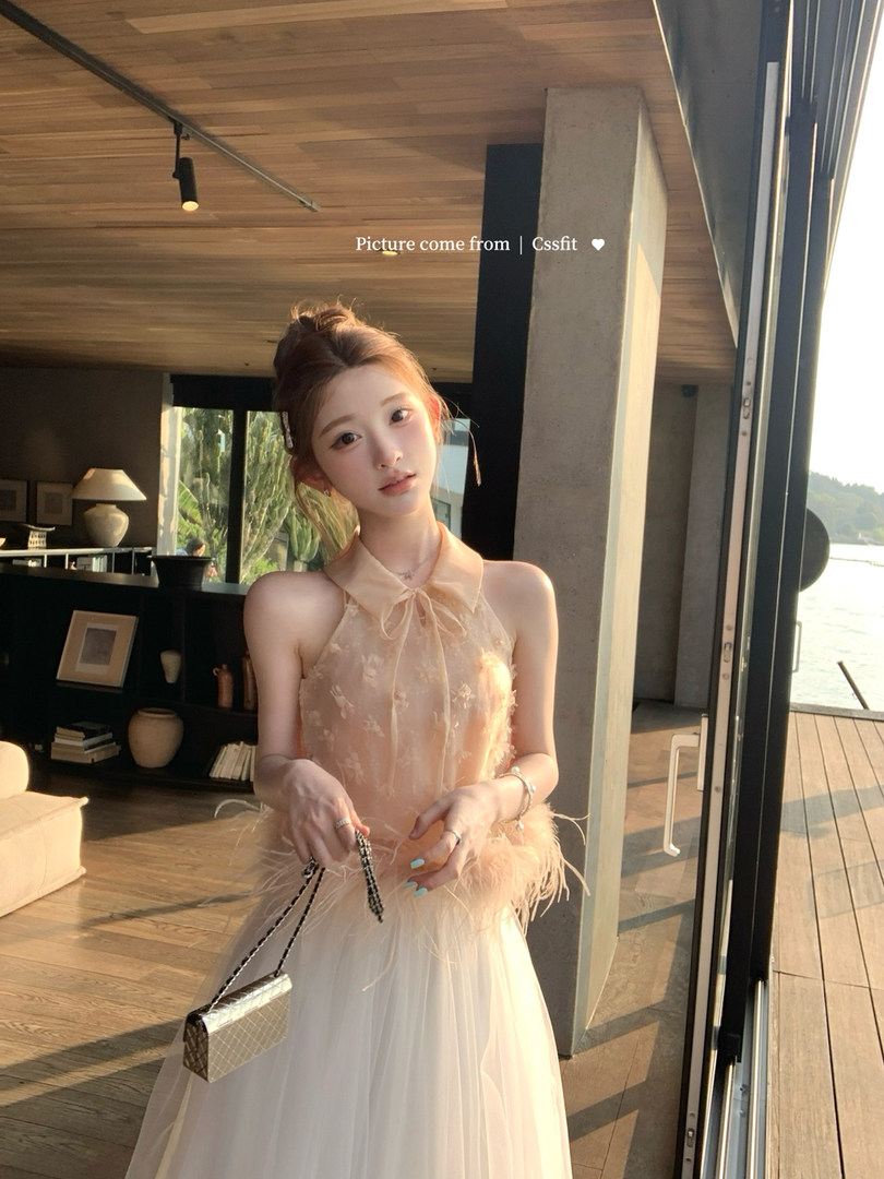 Woman wearing a light peach elegant halter dress with a flowing skirt and feather trim
