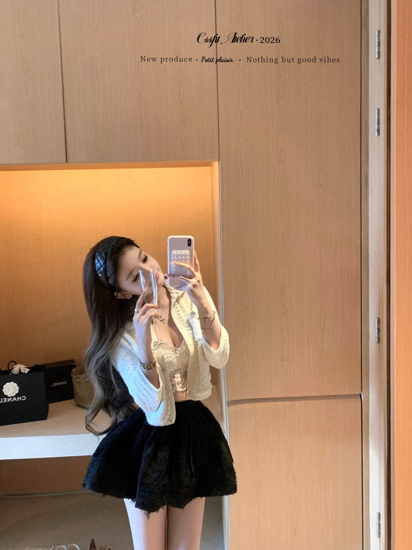 Mirror selfie of a woman wearing a light cardigan, lace top, and black mini skirt
