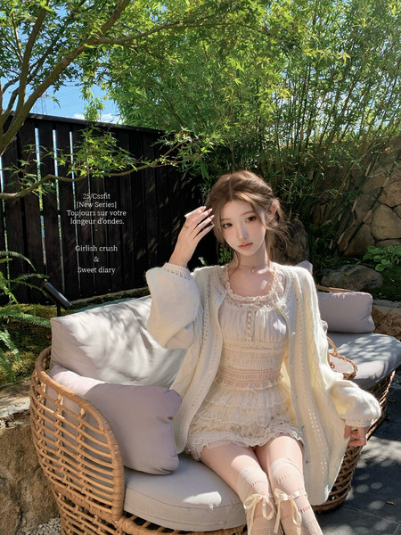 Woman wearing a cream lace dress and cardigan outdoors on a wicker sofa