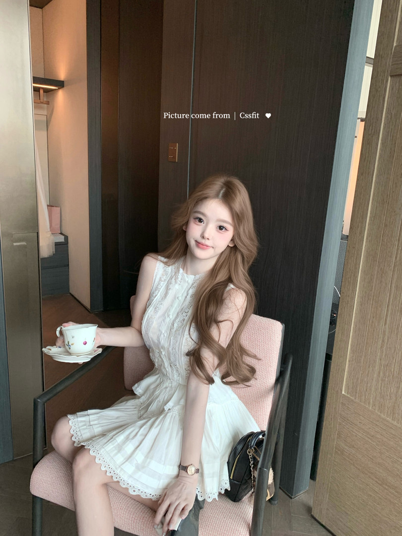 Woman wearing a white lace sleeveless dress while seated indoors