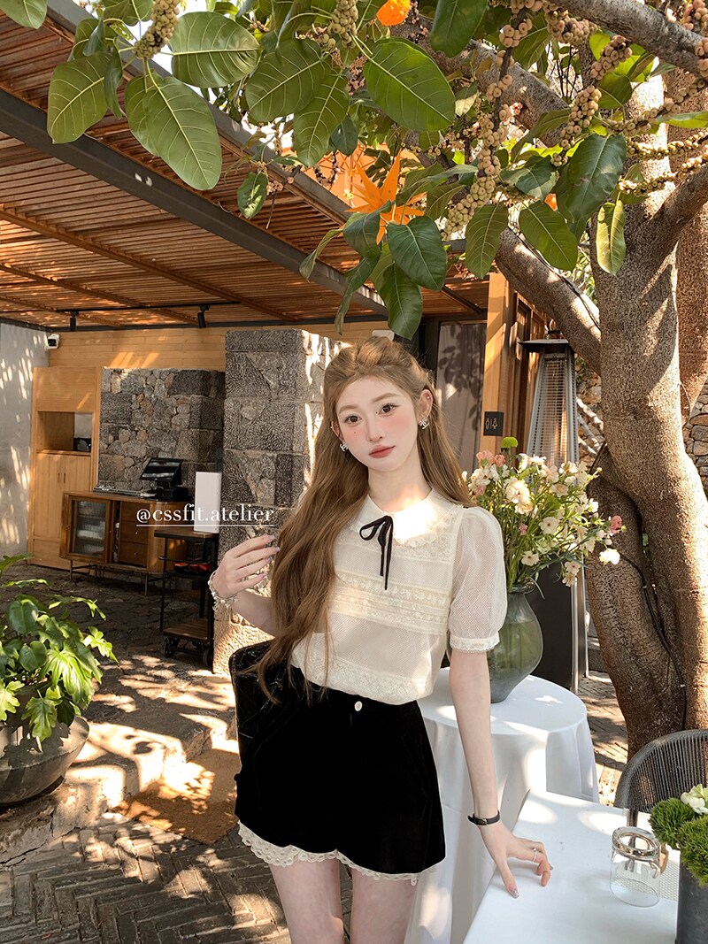 Model wearing a sheer white short-sleeve top and black lace-trim shorts outdoors
