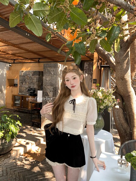 Model wearing a sheer white short-sleeve top and black lace-trim shorts outdoors