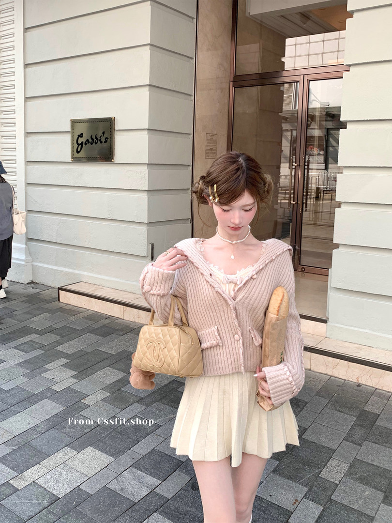 Pastel pink knit cardigan and cream pleated skirt worn by a model outdoors
