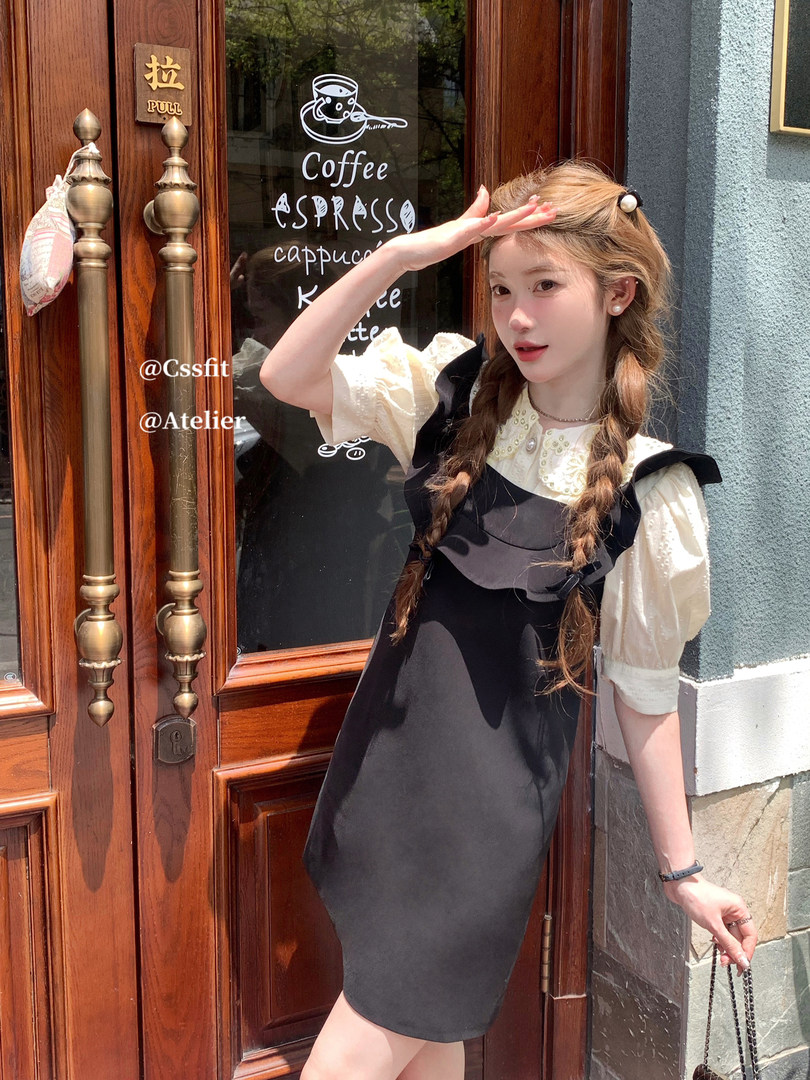 Woman modeling a black pinafore dress over a cream blouse outdoors