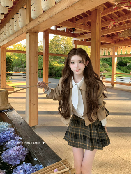 Young woman wearing a beige jacket, white blouse, and plaid pleated skirt outdoors