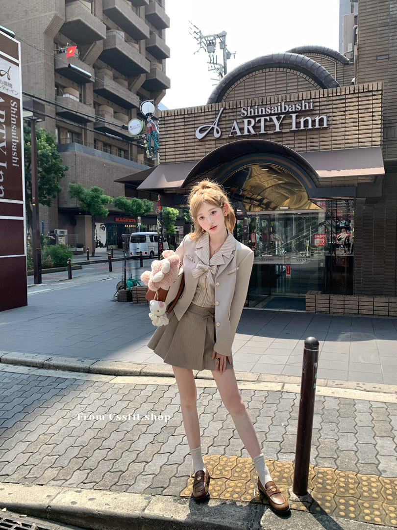 Young woman wearing a beige preppy outfit with pleated skirt and loafers outdoors
