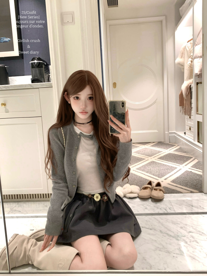 Woman wearing a gray cardigan, white top, and black skirt in a mirror selfie