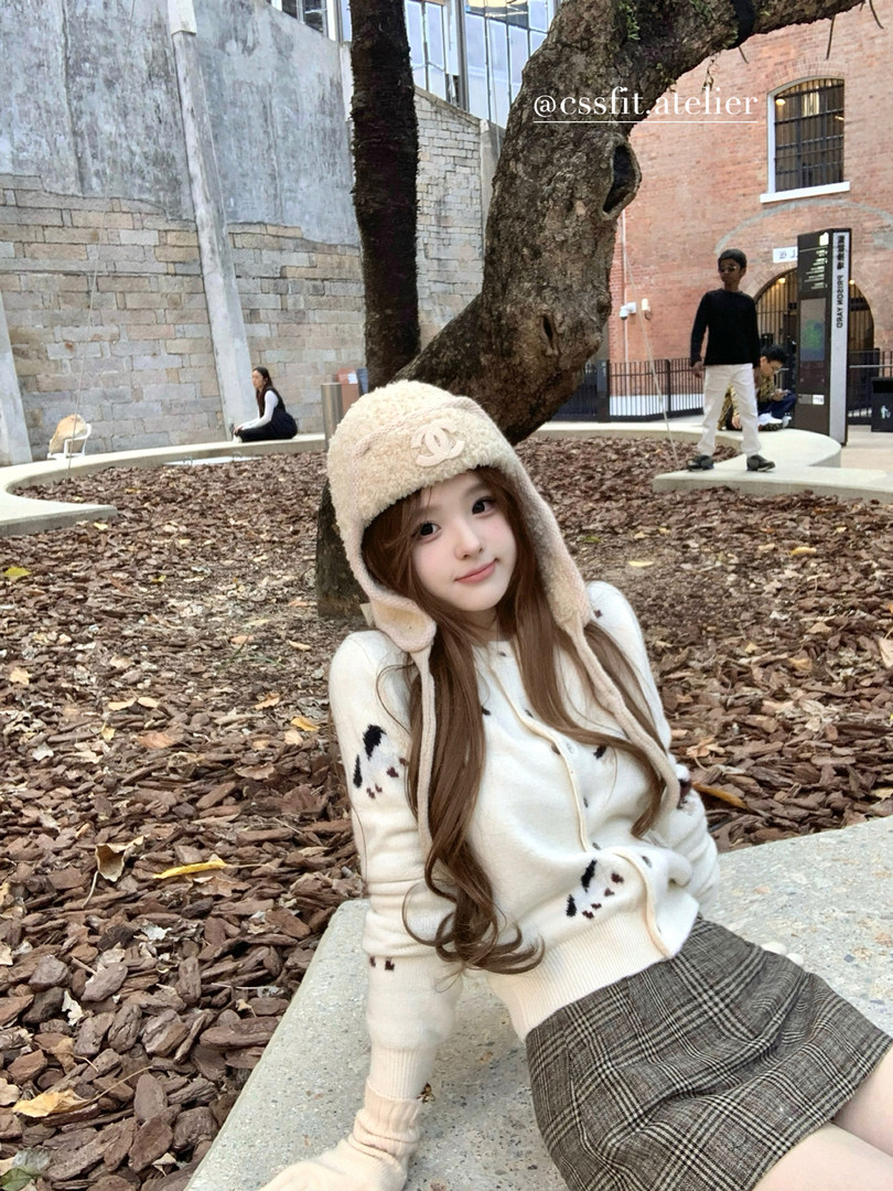 Woman wearing a cream fuzzy earflap hat and matching knit sweater with a plaid skirt