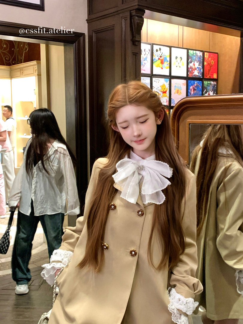 Model wearing a beige tailored blazer with a large white bow and lace cuffs
