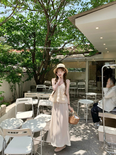 Woman wearing a cream lace top and long beige skirt with a straw hat outdoors
