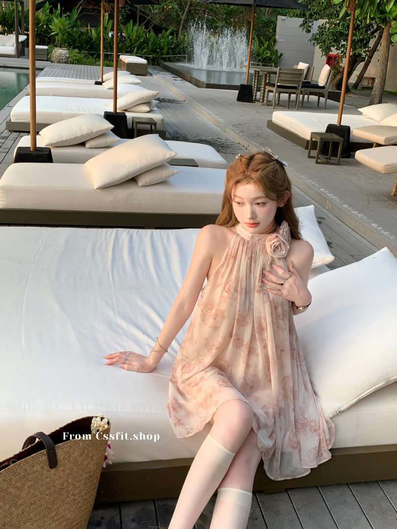 Woman wearing a light floral halter dress by a poolside cabana
