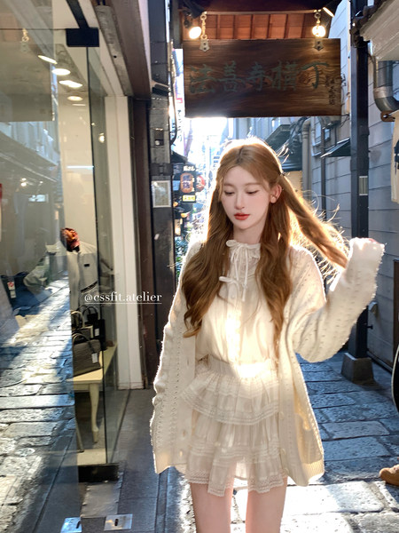 Woman wearing a light white ruffled cardigan and layered skirt outfit on a street