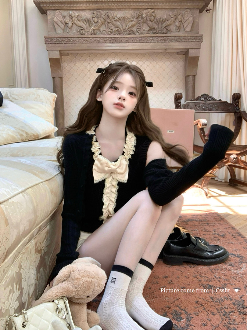 Black long-sleeve ruffled cardigan with cream bow detail worn by a model