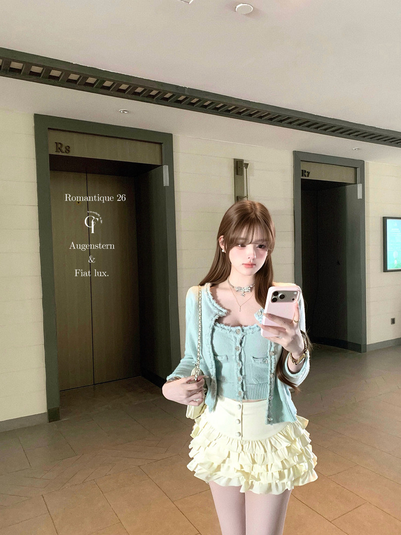Woman wearing a pastel blue cardigan and cream ruffled mini skirt in a mirror selfie
