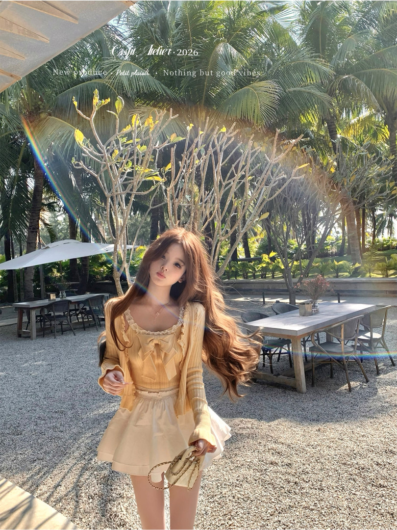 Woman wearing a light yellow ribbed cardigan and cream skirt outdoors in a tropical setting