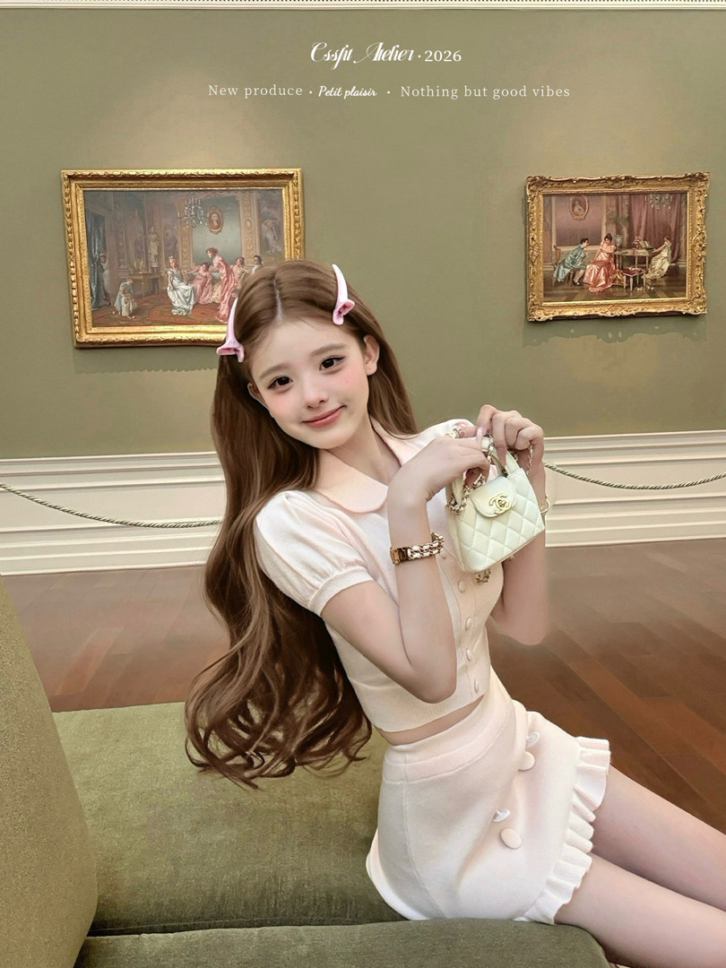 Model wearing a cream two-piece outfit and holding a small quilted handbag.