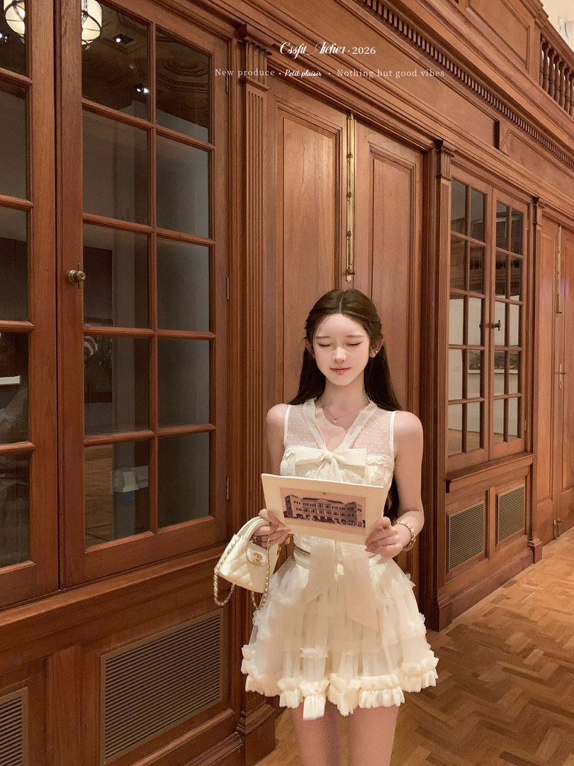 Woman wearing a white frilly sleeveless dress holding a handbag indoors