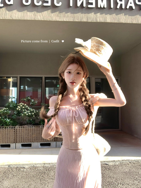 Model wearing a light pink off-shoulder dress and straw hat outdoors