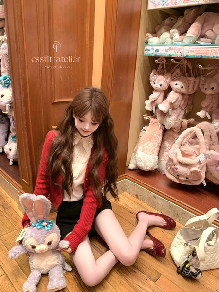 A girl wearing a red cardigan and white blouse, seated in a boutique with plush bunny bags and accessories around her