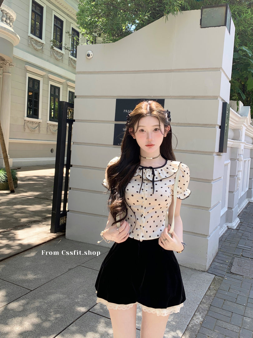 Model wearing a cream polka dot ruffle blouse with black shorts outdoors