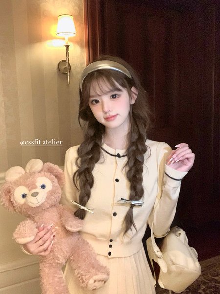 Model wearing a cream cardigan and pleated skirt with a headband