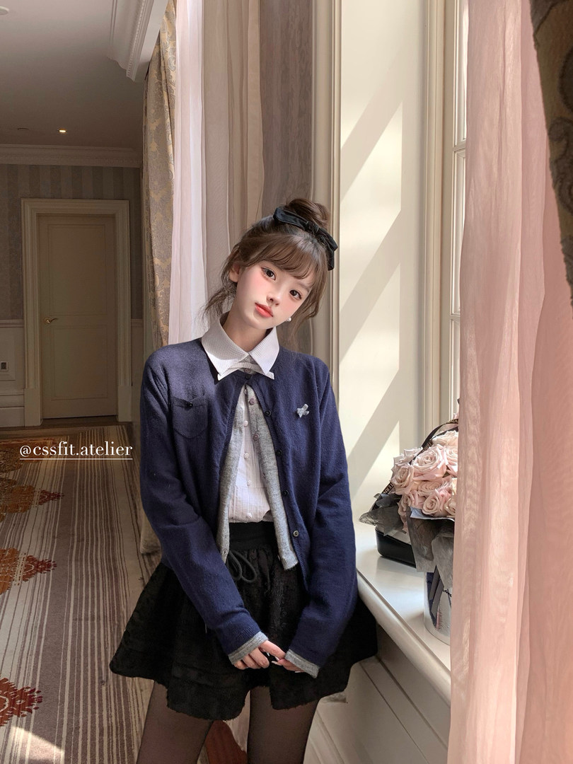 Young woman wearing a navy cardigan over a blouse and black skirt indoors