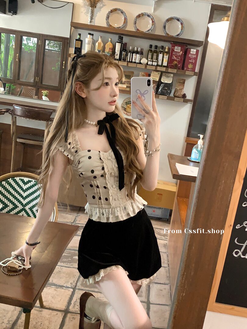 Woman modeling a beige polka dot ruffled top with black velvet skirt in a mirror selfie