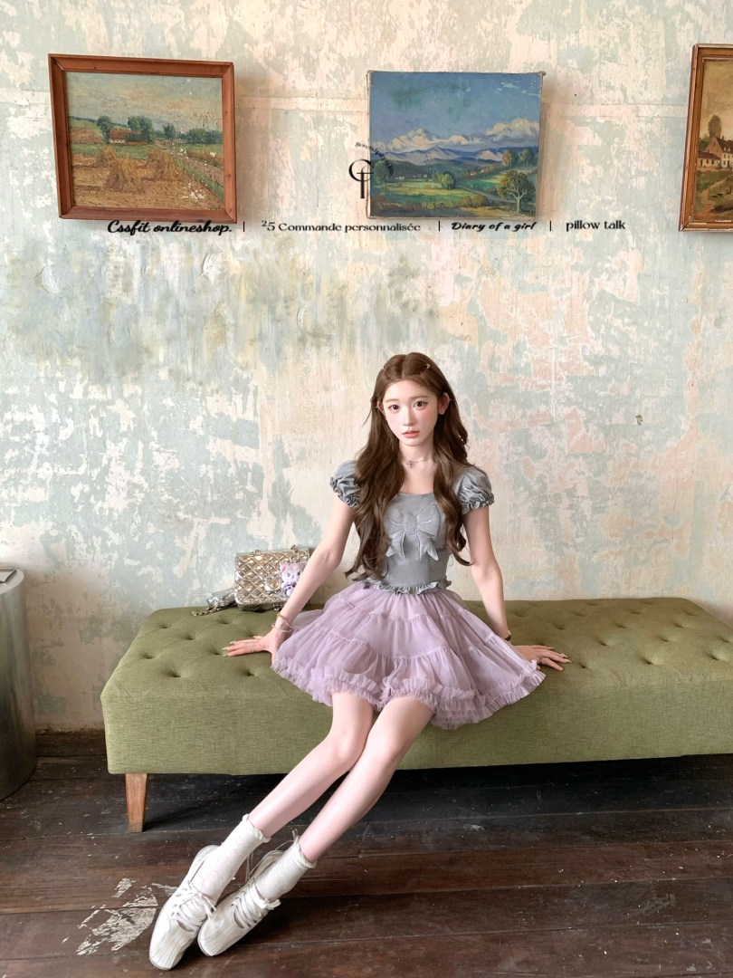 Model wearing a gray puff-sleeve top with a lilac ruffled skirt and white shoes