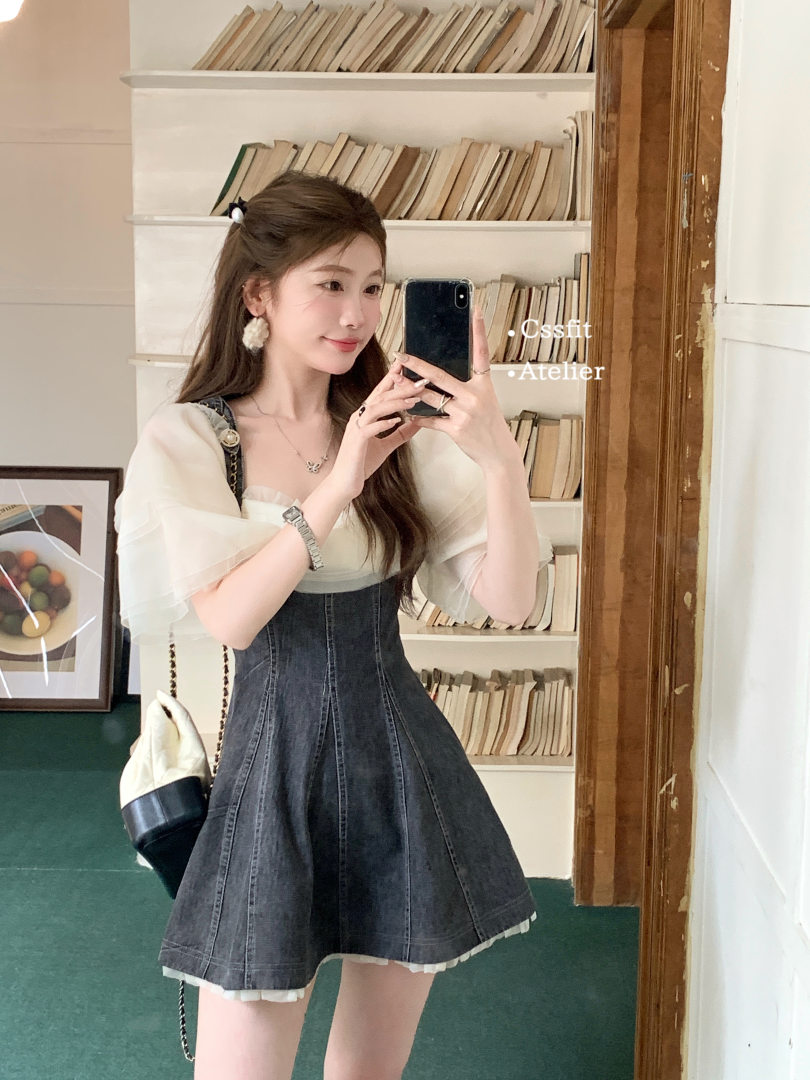 Woman wearing a dark denim mini dress with a white puff-sleeve top in a mirror selfie