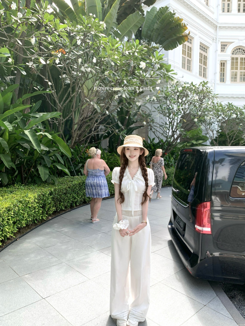 Woman wearing a white flowing two-piece outfit and straw hat outdoors
