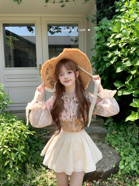 Woman wearing a floral blouse and white skirt with a straw sun hat outdoors
