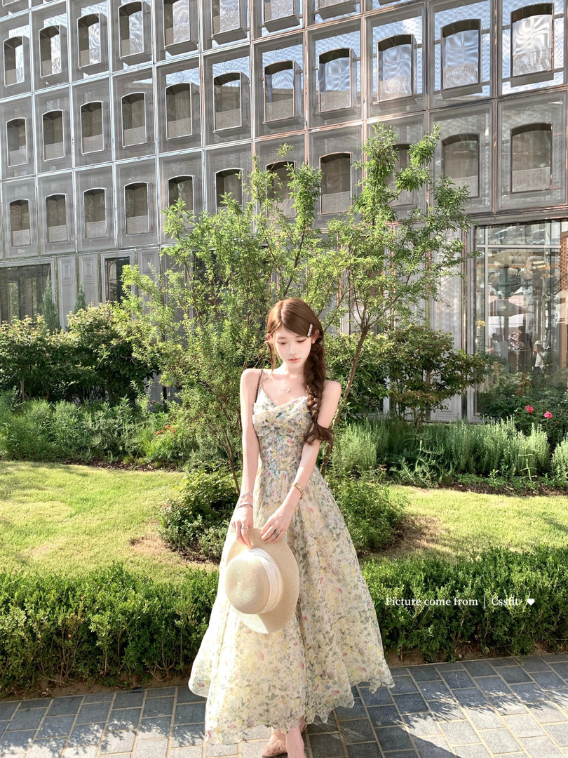 Woman wearing a light floral maxi dress outdoors while holding a straw hat