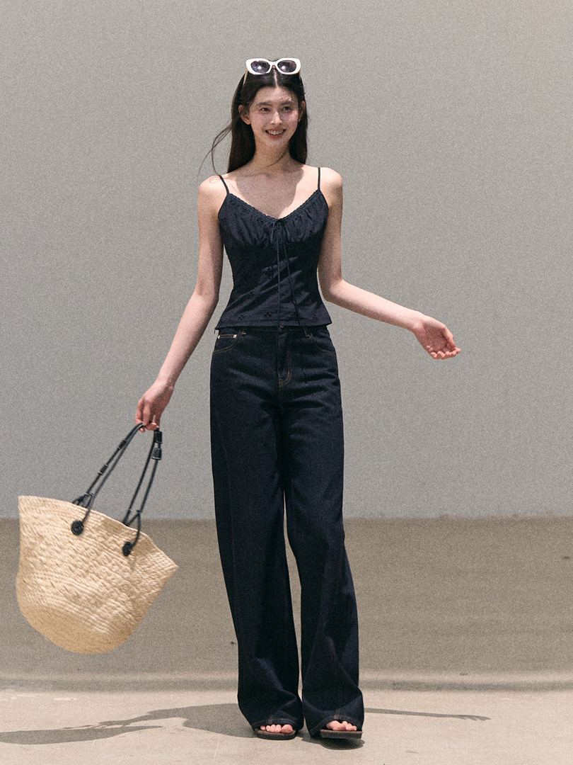Model wearing a black spaghetti-strap top with wide-leg dark jeans and a straw tote bag