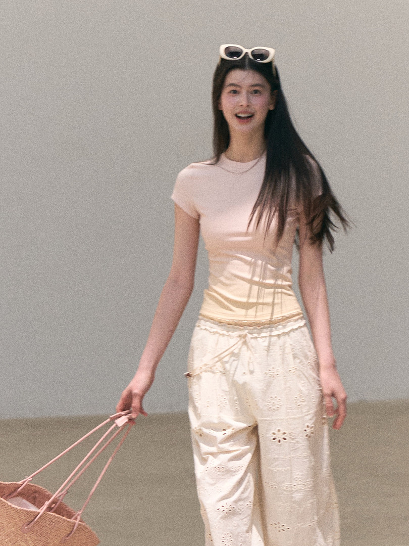 Model wearing a light cream outfit with eyelet pants and a pink tote bag