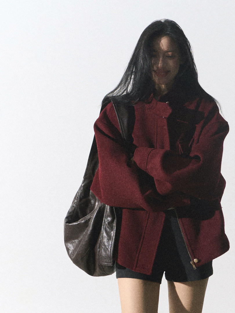Model wearing a burgundy and black oversized jacket with a large black leather bag