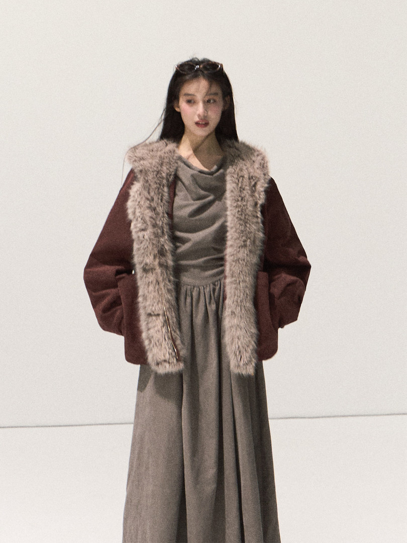 Model wearing a long fur-trimmed coat over a muted dress