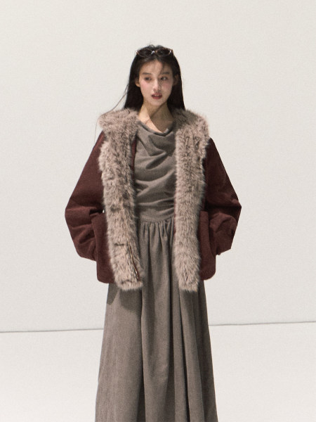 Model wearing a long fur-trimmed coat over a muted dress