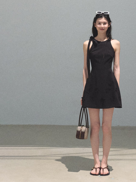 Model wearing a black sleeveless dress with sandals and a small handbag