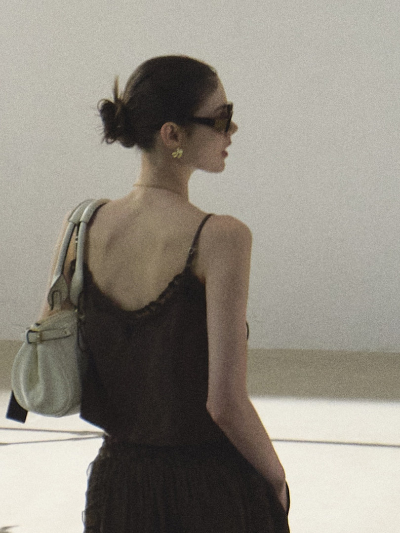 Woman wearing a black spaghetti-strap dress with a light shoulder bag