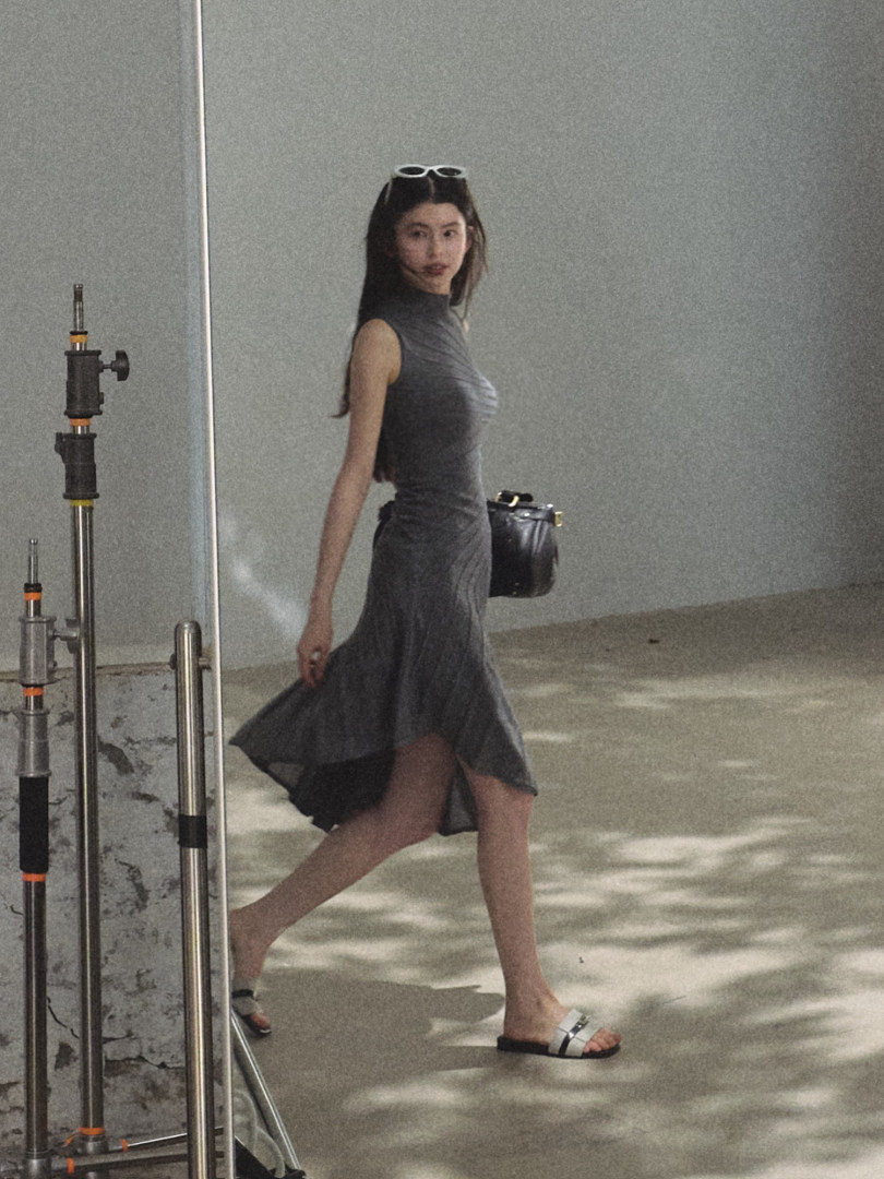 Model wearing a dark sleeveless midi dress with sandals and a small black handbag