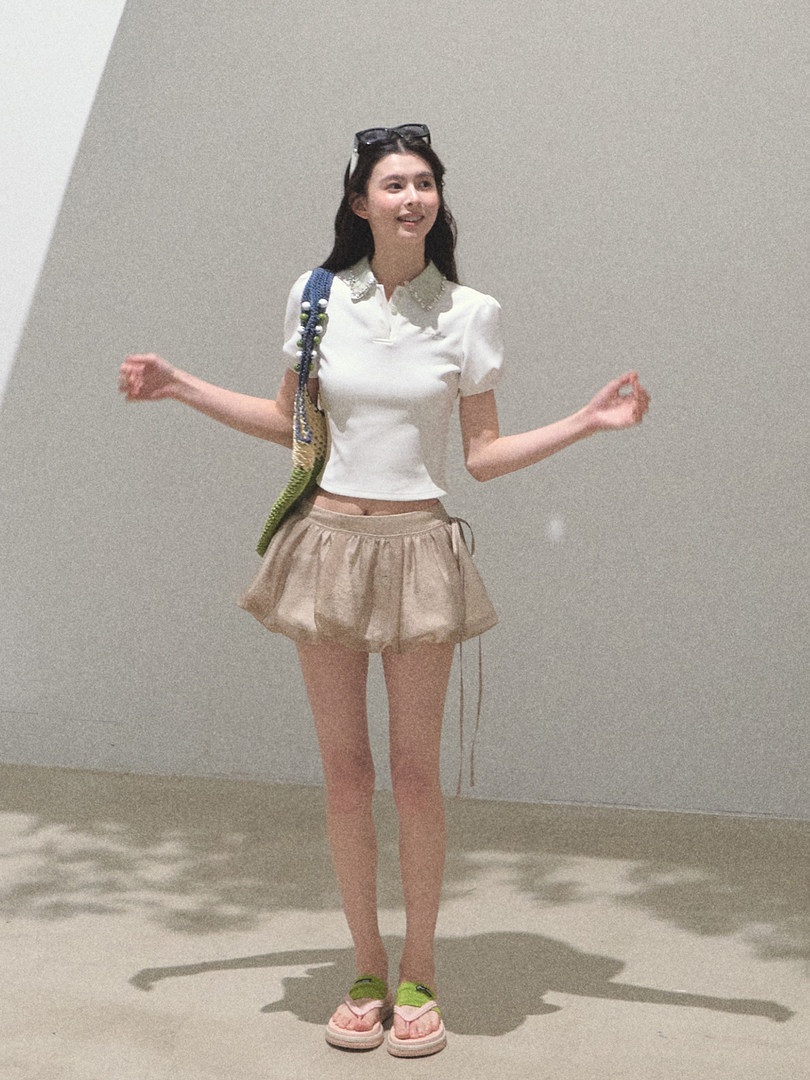 Woman wearing a white short-sleeve top, beige mini skirt, and pink-green sandals