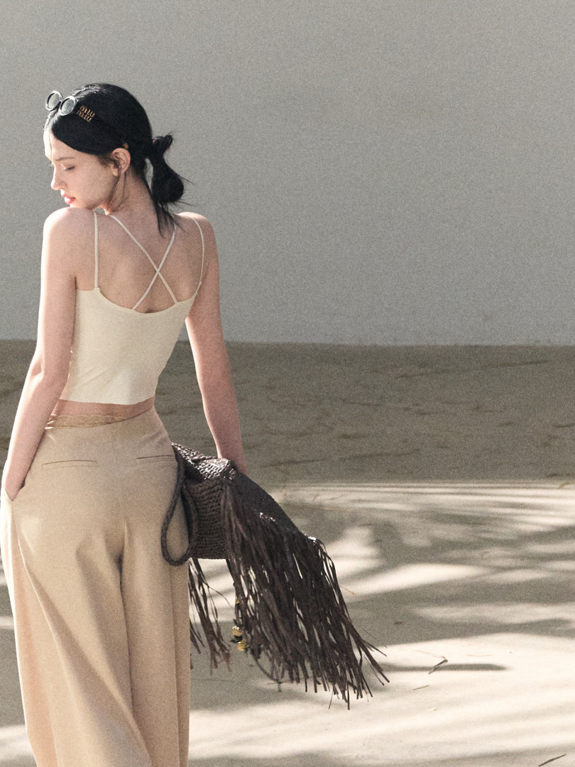 Model wearing a cream strappy back top with matching wide-leg skirt and carrying a fringed bag