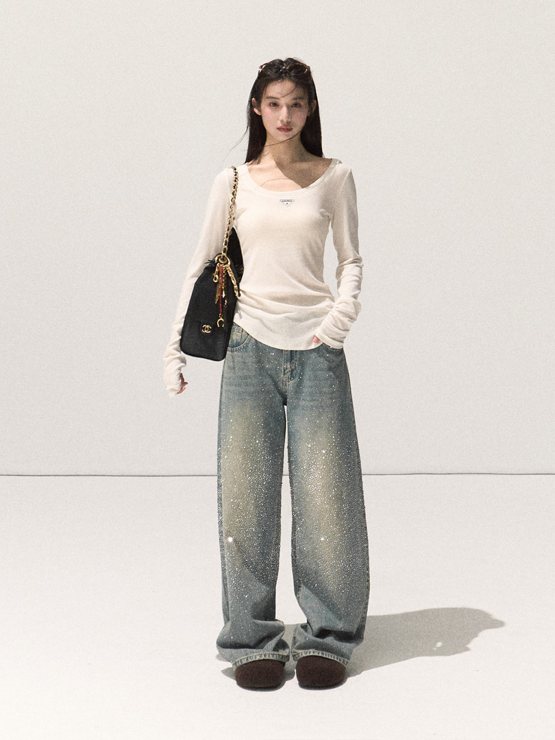 Model wearing a white long-sleeve top with sparkly wide-leg jeans and a black shoulder bag